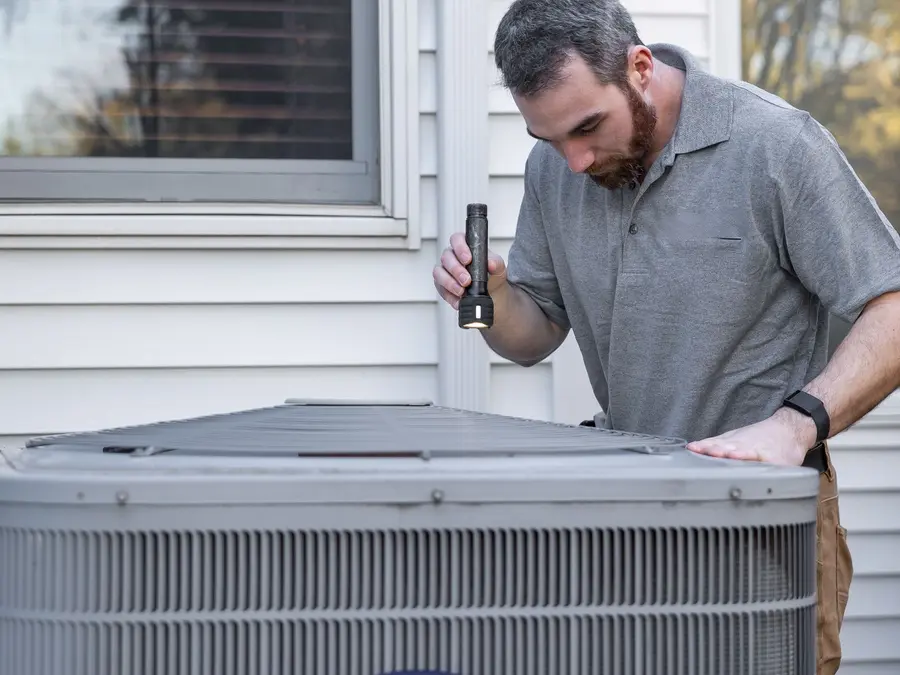 Technician checking an outdoor AC condenser unit with a flashlight