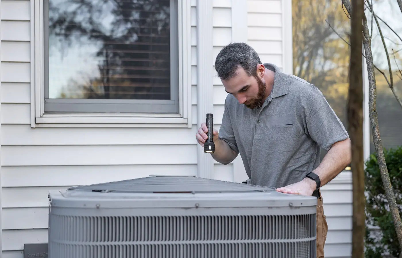 Technician inspecting an outdoor AC condenser unit beside a home